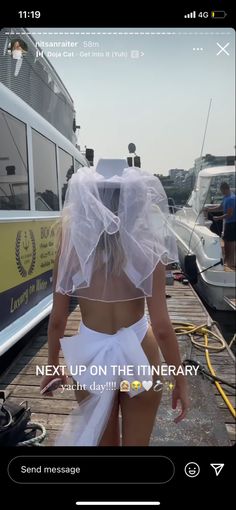 a woman wearing a white wedding dress and veil walking on a dock with boats in the background