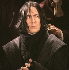 a man with long hair wearing a black coat and holding his hand on his chest