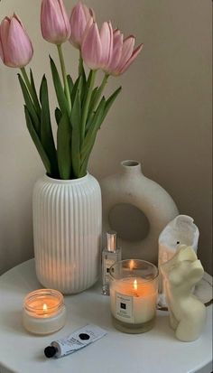 pink tulips in a white vase on a table with candles and other items