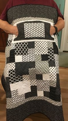 a man is holding up a quilt made from black and white squares on a table