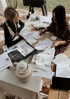 two women sitting at a table covered in papers