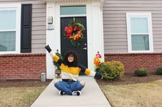 a woman sitting on the ground in front of a house with her arms up and legs crossed