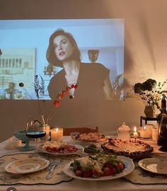 a table is set with food and candles for a movie viewing event in front of a large screen