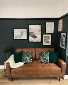 a brown couch with green pillows and pictures on the wall