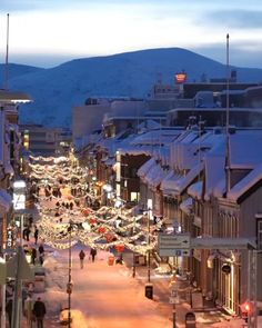 a city street with cars parked on the side of it and christmas lights hanging from the buildings