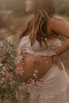 a woman standing in a field with flowers on her stomach and wearing a white dress