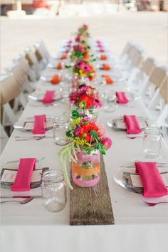 a long table is set with pink napkins and flowers in vases on it