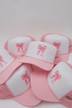 pink and white baseball caps with bows on the front are stacked up in a pile