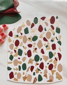 a piece of paper with gold foil on it next to some red and green leaves