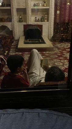 two people sitting on a couch looking at a book in a room filled with furniture