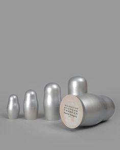 a group of silver vases sitting next to each other on a gray surface with a wooden disc in the middle