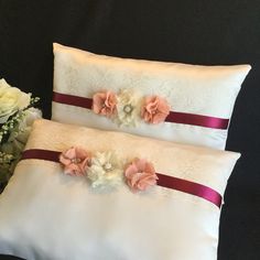 two pillows with flowers on them sitting next to a vase filled with white and pink flowers