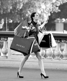 black and white photograph of a woman carrying shopping bags while walking down the street with her hand up in the air