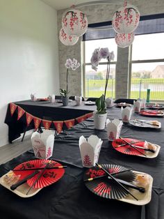 a black table topped with red and white paper fans next to vases filled with flowers