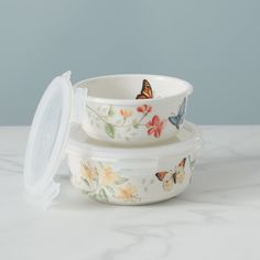 three bowls with butterfly designs on them sitting on a marble countertop next to a plastic container