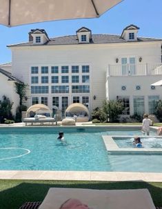 people are swimming in an outdoor pool next to a large white house