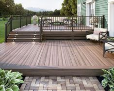 a wooden deck with chairs on it next to a green house and some plants in the foreground