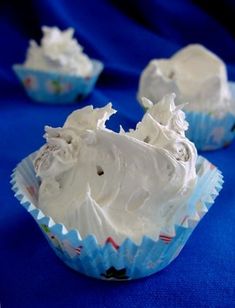 three cupcakes with white frosting sitting on a blue cloth