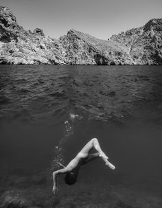 a person floating in the water near some mountains and rocks, with their legs spread out