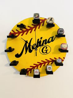 a yellow clock with black letters and baseballs on the numbers is shown in front of a white wall