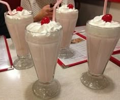 three glasses filled with ice cream and topped with cherries on a table in front of people