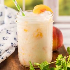 a mason jar filled with ice and topped with a peach slice, sitting on top of a wooden cutting board