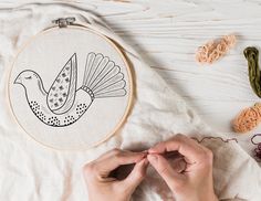 a woman is stitching a bird on a piece of cloth next to some crochet