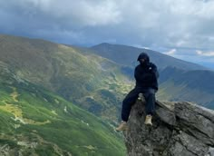 a man sitting on top of a rock next to a lush green valley below him