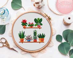 a cross stitch pattern with potted plants and scissors on the table next to it