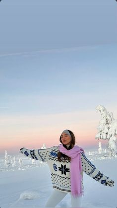 a woman is standing in the snow with her arms spread out and wearing a scarf