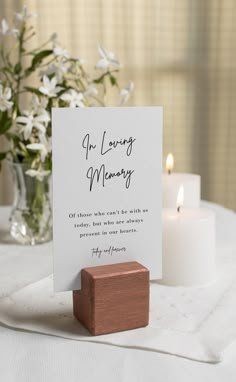 a wooden block sitting on top of a table next to a vase with white flowers