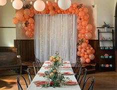 a long table is set up with orange and white balloons