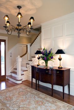 a living room filled with furniture and a chandelier hanging from the ceiling over a wooden table