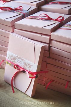 many pink boxes with red ribbons tied around them on a wooden table next to each other