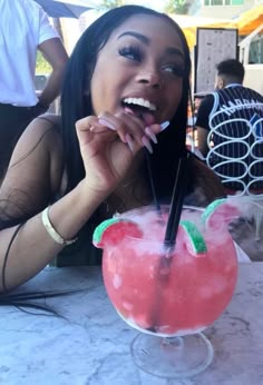 a woman sitting at a table with a drink in front of her and tongue sticking out