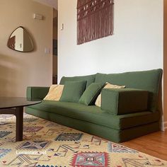 a green couch sitting on top of a wooden floor next to a table and mirror