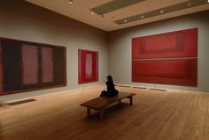 a person sitting on a bench in an art gallery looking at two large red paintings