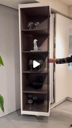 a man standing in front of a tall cabinet with wine glasses on the bottom shelf