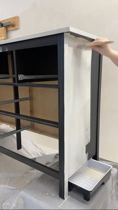 a person is painting a cabinet with white paint on the wall and another hand reaching for it