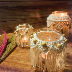 three candles are sitting on a table with some yarn and beads hanging from the candle holders