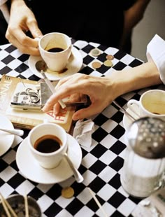 two people sitting at a table with cups of coffee in front of them and an open book on the table