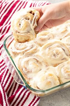 a person holding a cinnamon roll in a glass baking dish