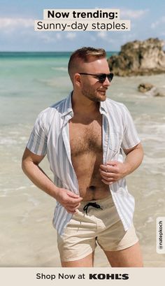 a man standing on the beach with his shirt off and sunglasses on, wearing shorts