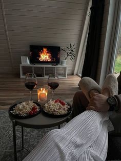 a man sitting in front of a fire with two plates of food on the table