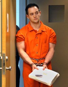 a man in an orange prison uniform holding a box and chain around his waist as he stands next to a door