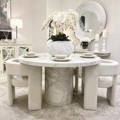 a white table with four chairs around it and a vase filled with flowers on top