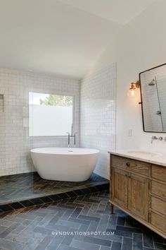 a large white bath tub sitting next to a wooden cabinet in a bathroom with tile flooring