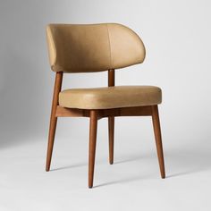 an upholstered chair with wooden legs and a tan leather seat pad on the back