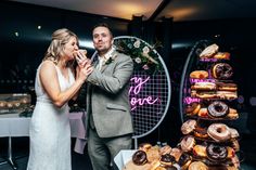 a bride and groom standing in front of a display of doughnuts at their wedding reception