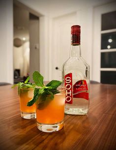 two glasses filled with alcohol sitting on top of a wooden table next to a bottle